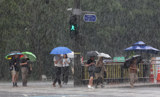 People with umbrellas cross a crosswalk near Gwanghwamun in Jongno District, central Seoul, as a heavy rain advisory was issued for the city on Tuesday. [YONHAP]