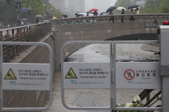 People walk past the Cheonggyecheon, a stream that flows through downtown Seoul, which was closed for safety reasons following a heavy rain advisory on Tuesday. [YONHAP]