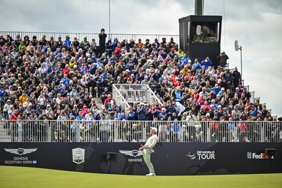 Rory McIlroy smiles after making a winning birdie putt on the 18th hole green while fans celebrate in the grandstand during the final round of the Genesis Scottish Open at The Renaissance Club on July 16, 2023 in North Berwick, Scotland. [GETTY IMAGES]