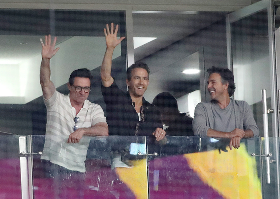 Hugh Jackman, left, and Ryan Reynolds wave to fans with director Shawn Levy in a game between the LG Twins and Kiwoom Heroes at Gocheok Sky Dome in Guro District, western Seoul on July 3. [NEWS1]