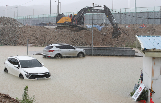 An excavator scoops water out from a flooded construction site in Daejeon on Monday morning. [NEWS1]