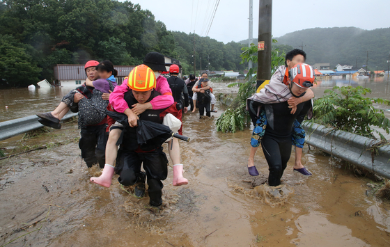 Firefighters carry stranded residents as a part of efforts to evacuate 36 villagers in Yongchon-dong in Seo District, Daejeon, after overnight rain flooded the area on Wednesday. Fire authorities mobilized 13 pieces of equipment and 73 personnel to rescue residents. [NEWS1]