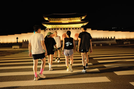 Runners make their way toward Gwanghwamun, illuminated by yellow light, to start their 8-kilometer run. [HAN STRIDE]