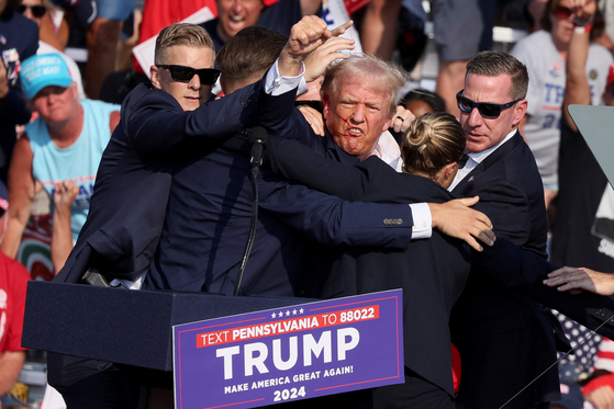 Former U.S. President Donald Trump, center, pumps his fist at the crowd after a shooting at a campaign rally in Butler, Pennsylvania, Saturday. The Republican candidate is seen with blood on his face surrounded by Secret Service agents as he is taken off the stage. [REUTERS/YONHAP]