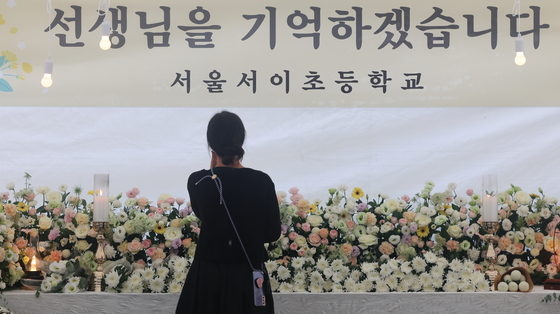 A woman pays condolences at a memorial altar installed at Seo 2 Elementary School in Seocho District in southern Seoul on Thursday, marking the anniversary of the death of a young teacher who died by suicide after allegedly experiencing harassment from students’ parents. [NEWS1]