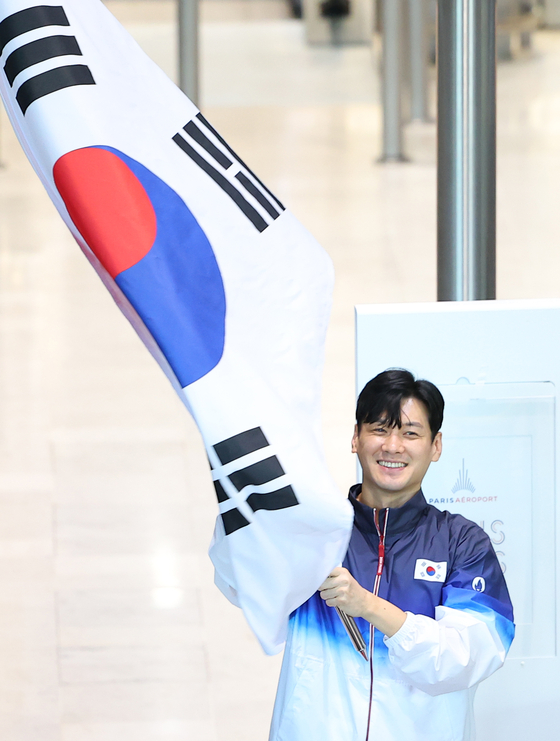 Fencer Gu Bon-gil, an Olympic gold medalist, waves the national flag, Taegeukgi, as the South Korean main delegation for the Paris Olympics arrives at Paris Charles de Gaulle Airport in France on Saturday, ahead of the Summer Games. [YONHAP]