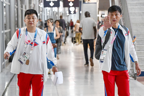 A member of the North Korean delegation for the 2024 Paris Olympics holds up his hand at reporters as he arrives at Paris Charles de Gaulle Airport in France on Saturday. [JOINT PRESS CORPS]