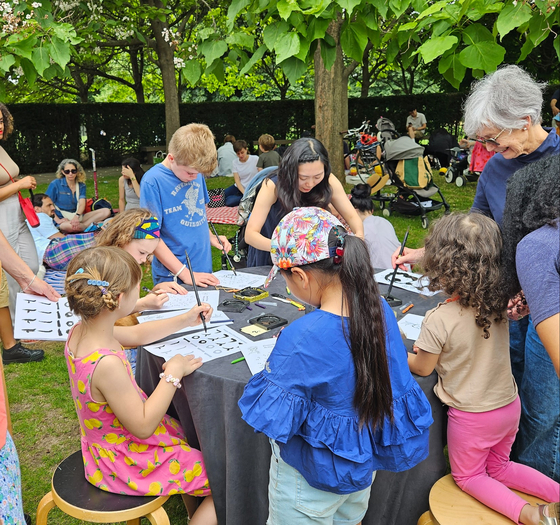 Visitors try out Korean calligraphy during the “Pavilion Family Day” event at the Serpentine Pavilion on Sunday. [KOREAN CULTURAL CENTRE UK]