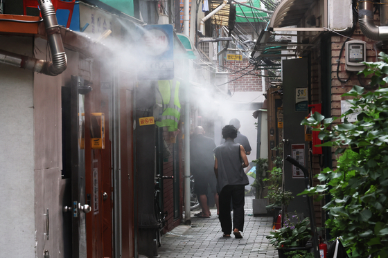 A person cools off the heat under a cooling fog system in an alley in a shanty town in Donui-dong, Jongno District in central Seoul, on Wednesday. [YONHAP]