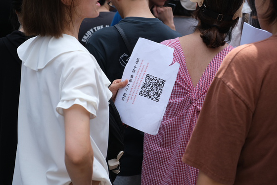 A TMON customer holds a sheet with a QR code that allows online registration for a waiting ticket for refunds. [CHO YONG-JUN]