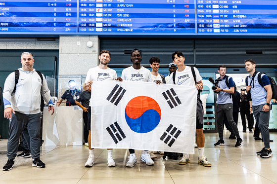 Tottenham Hotspur's Ben Davies, left, Yves Bissouma and Son Heung-min hold the Korean flag under a departures board. [COUPANG PLAY]