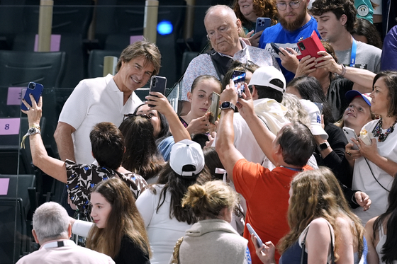 Actor Tom Cruise, left in white, poses for pictures with fans as he attends the women's artistic gymnastics qualification round at the Paris Olympics on in Paris. [AP/YONHAP]