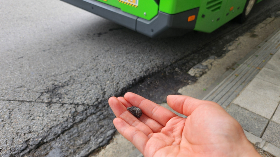 A pedestrian shows a piece of cracked asphalt flicked out from a pothole near a bus stop in central Seoul on Thursday. [KIM SEO-WON]