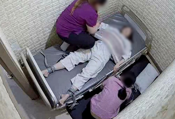 A nursing assistant and caregiver restrain a patient on the bed in a psychiatric hospital in Bucheon, Gyeonggi, on May 27. [YONHAP]