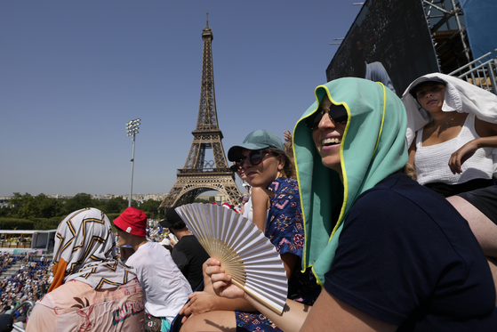 Stephanie Touissaint, foreground, uses a fan to keep cool in the sweltering heat at Eiffel Tower Stadium during a beach volleyball match between Cuba and Brazil in Paris on Tuesday.  [AP/YONHAP]