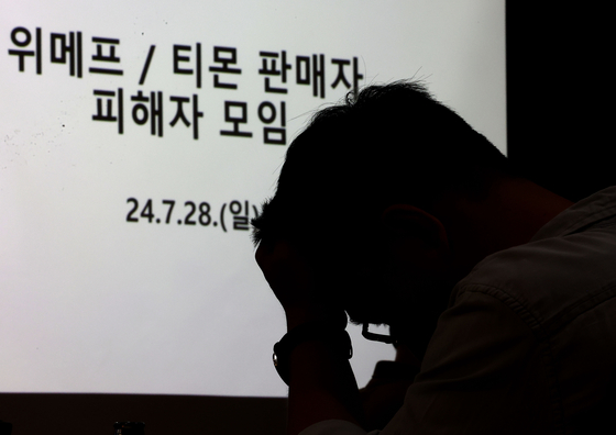 A merchant listed on Qoo10-owned e-commerce platforms TMON and WeMakePrice grabs his head at a meeting for the sellers held at Gangnam District, southern Seoul on Sunday. [YONHAP]
