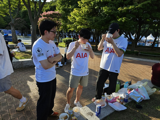 Football fans wearing Tottenham Hotspur jerseys eat snacks in front of Seoul World Cup Stadium in western Seoul on Wednesday ahead of a Coupang Play Series match between Spurs and Team K League. [PAIK JI-HWAN]