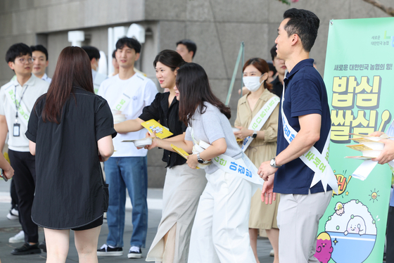 Deloitte Korea employees pass out leaflets and cooked rice produced by the National Agricultural Cooperative Federation, better known as NongHyup, to pedestrians as part of the two firms' collaborative campaign encouraging the consumption of rice for breakfast in Yeongdeungpo District, western Seoul, on Wednesday.