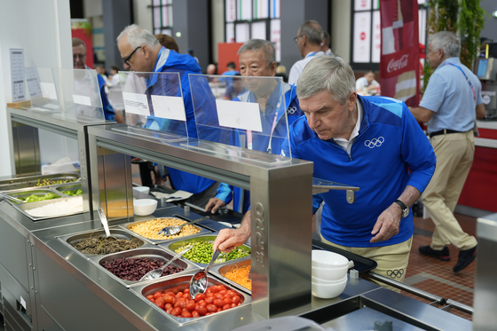 Thomas Bach, president of the International Olympic Committee, tries food from a salad bar while touring the Olympic Village ahead of the Summer Olympics in Paris on July 22. [AP/YONHAP]
