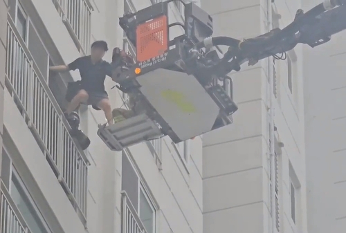 A resident is being rescued by a firefighter on a balcony of an apartment in Incheon after smoke suffused the complex following a fire caused by a Mercedes-Benz EV explosion in an underground parking lot on Thursday. [INCHEON FIRE DEPARTMENT]