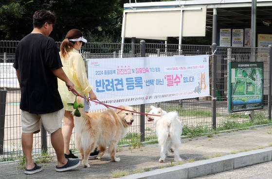 Pet owners walk their dogs in the World Cup Park in Mapo District, western Seoul, on Sunday in front of a banner that says registering dogs is required as the Seoul Metropolitan Government announced that the city will waive fines for unregistered pets from Monday until Sept. 30. [NEWS1] 