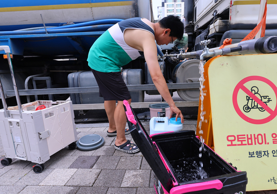A resident of an apartment complex in Incheon that suffered a massive fire from an EV explosion in an underground parking lot takes water from a water truck on Monday. Around 480 households have been suffering from electricity and water outages in the aftermath of the fire. [YONHAP] 