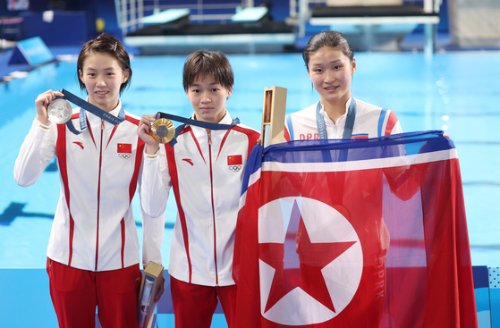 Kim Mi-rae of North Korea, right, holds up the North Korean flag after winning the bronze medal in the women's 10-meter platform diving event at the Paris 2024 Olympics on Tuesday. [YONHAP]