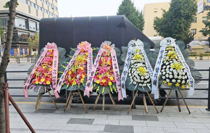 Wreaths of flowers displaying messages of BTS's Suga to leave the band in front of HYBE's headquarters in Yongsan District, central Seoul, on Tuesday. [SCREEN CAPTURE]