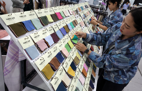  Employees hang textile samples at a trade show at Coex in southern Seoul on Wednesday. [YONHAP]