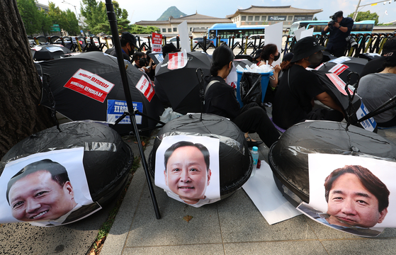 The faces of Qoo10 CEO Ku Young-bae, right, TMON CEO Ryu Kwang-jin and WeMakePrice CEO Ryu Hwa-hyeon are attached to black umbrellas as part of a protest staged by merchants and customers affected by the Qoo10 e-commerce platforms' liquidity crisis in front of the Financial Services Commission headquarters in Jongno District, central Seoul, on Sunday. [YONHAP]