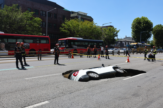 First responders oversee a site where a sudden road sinkhole swallowed a Tivoli SUV in Seodaemun District, western Seoul on Thursday. [YONHAP]