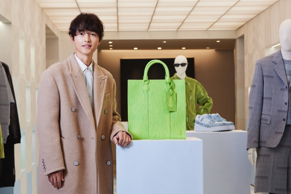 Actor Song Joong-ki poses wearing a coat and stands next to a bag from Louis Vuitton's new 2025 Spring/Summer collection line, inspired by the late dansaekhwa, or Korean monochrome painting, master Park Seo-bo. [LOUIS VUITTON]