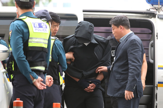 Police officials escort a man who opened an emergency exit door mid-flight on an Asiana Airlines plane to his warrant hearing at the Daegu District Court on May 28 last year. [NEWS1]