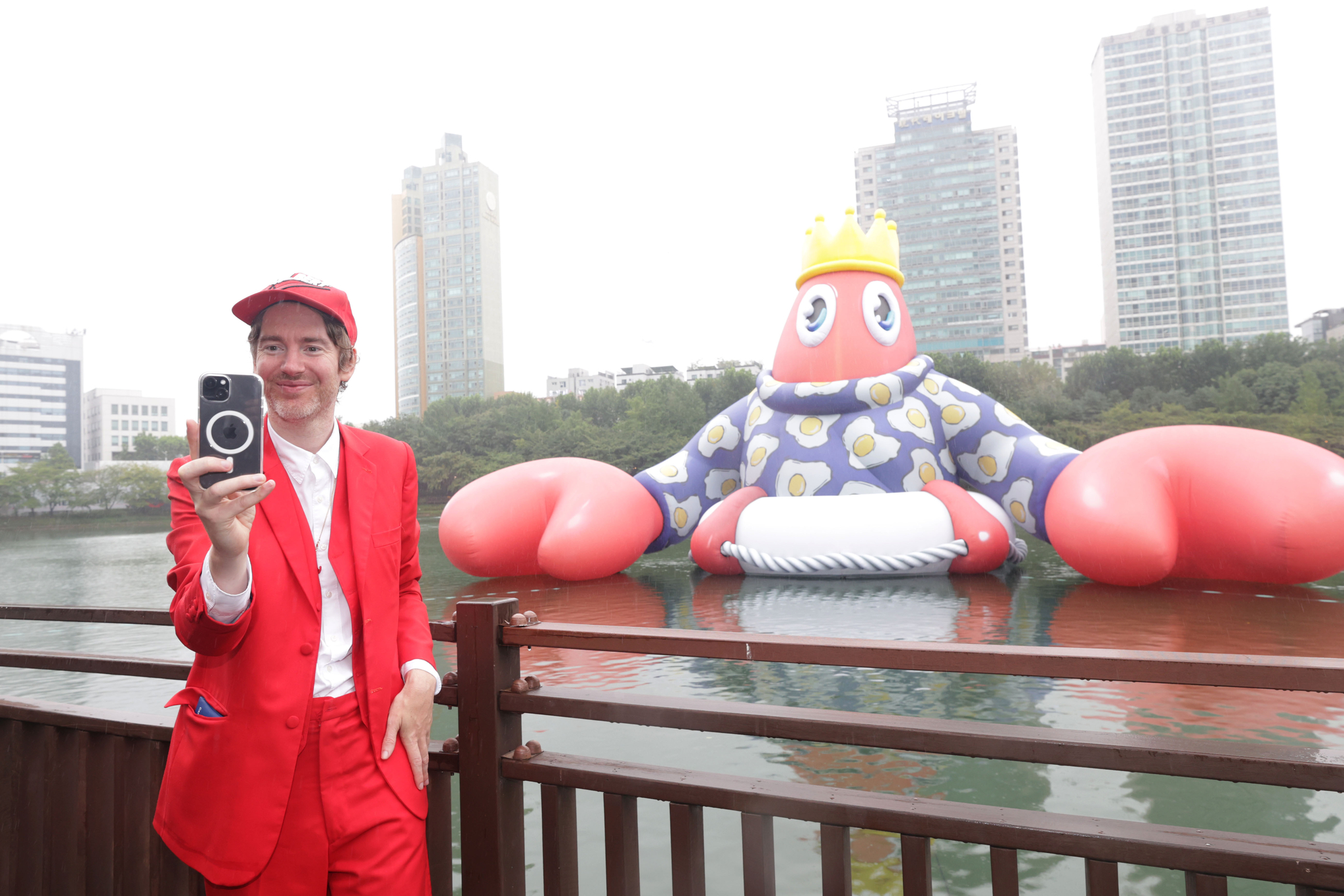 London-based Scottish artist Philip Colbert takes a photo in front of his lobster inflatable in Seokchon Lake in Songpa District, southern Seoul, on Friday. The installation piece is part of the ″Lobster Wonderland″ exhibition held in celebration of Lotte World Mall's 10th year anniversary of opening. [YONHAP]