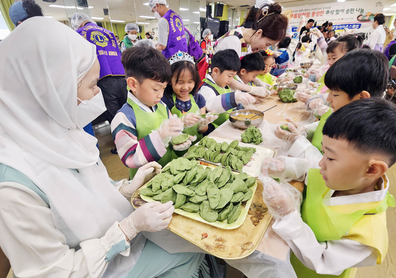 Volunteers and children in hanbok, or traditional Korean dress, make songpyeon (a moon-shaped Korean traditional rice cake) at an administrative welfare center in Buk District, Gwangju, on Tuesday, almost a week before the Chuseok harvest holiday begins. [BUK DISTRICT OFFICE]