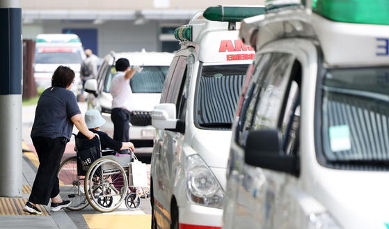 A patient and its guardian walk behind ambulances, which are lined up in front of a general hospital in Seoul on Tuesday. [NEWS1]