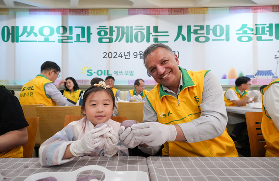 Refiner S-Oil CEO Anwar A. Al-Hejazi holds a songpyeon (traditional half-moon-shaped rice cake) with a child at the company's charity event.[S-OIL]