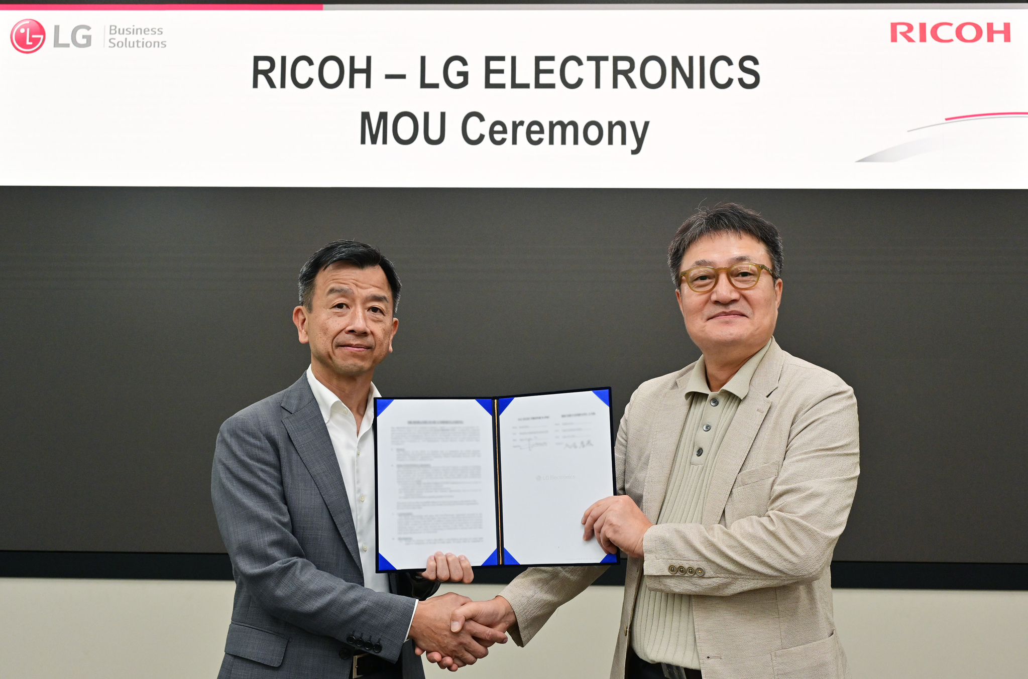 Paik Ki-mun, left, head of LG Electronics' information display business division, and Takahiro Irisa, president of digital services at Ricoh, shake hands in a signing ceremony in Seoul. [LG ELECTRONICS]