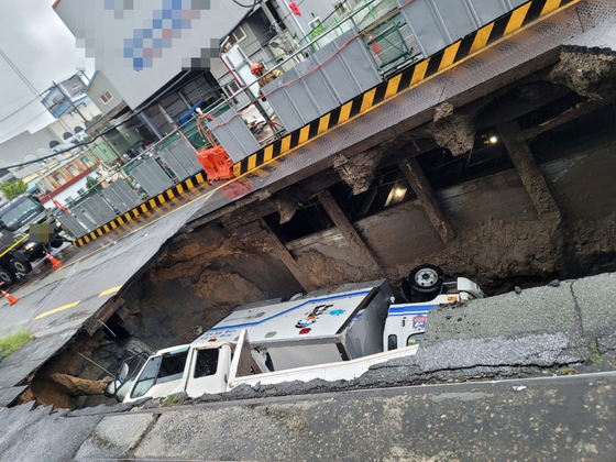 Two trucks fell into a sinkhole on a road in Sasang District in Busan on Saturday morning. [BUSAN METROPOLITAN POLICE AGENCY] 