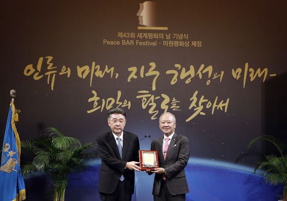 Choue Byung-tae, director of Kyung Hee International Foundation, right, poses for a photo with Choue In-won, chancellor of the Kyung Hee University System, after receiving an appreciation plaque during an event held as part of the annual Peace BAR Festival at the university's Peace Hall in Dongdaemun District, eastern Seoul, on Friday. [PARK SANG-MOON]