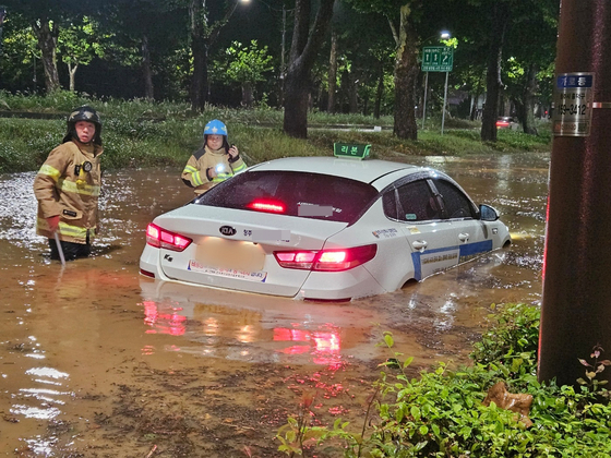 Firefighters take safety measures on a flooded road in North Chungcheong on Saturday morning. A taxi is also flooded by the rainwater. [NATIONAL FIRE AGENCY] 