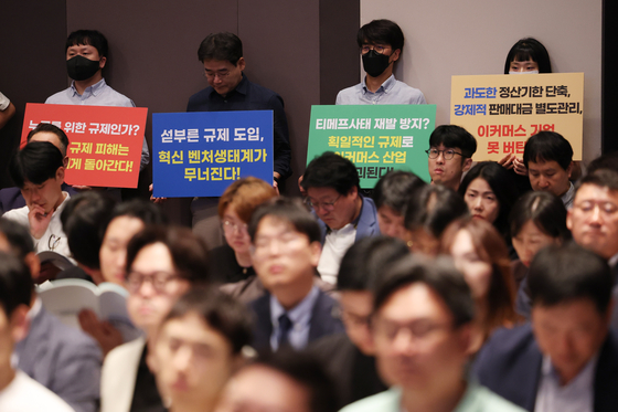 Protestors hold signs condemning the excessive regulation of the e-commerce industry during a public hearing regarding the payment crisis at TMON and WeMakePrice at the Korea Press Center in Jung District, central Seoul, on Monday. [YONHAP]