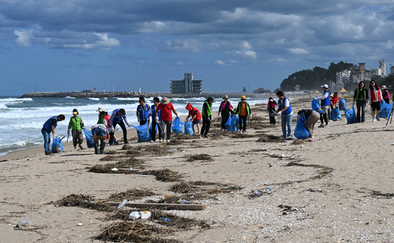 Volunteers clean up beach areas in the city of Gangneung, Gangwon, on Monday. Trash accumulated on white sand after heavy rain and high waves swept the coastline over the weekend. [YONHAP]