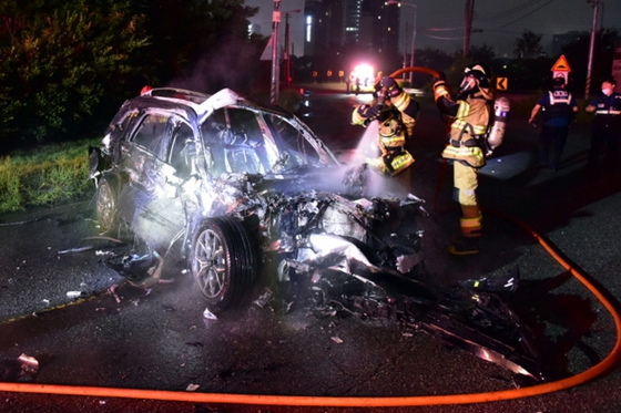 Firefighters extinguish a fire from a BMW that was completely burned after crashing into a trailer in Gwangsan District, Gwangju, on Sunday. [GWANGJU GWANGSAN FIRE STATION]