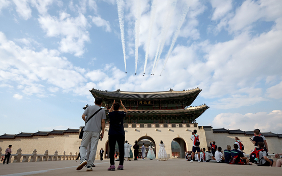 People take photographs as the Korean Air Force's aerobatic team Black Eagles conduct a rehearsal flyover above Gwanghwamun Gate in Jongno District, central Seoul, on Wednesday afternoon six days before the Armed Forces Day parade due to take place in the downtown area. [YONHAP]