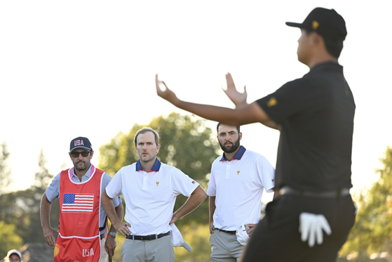 Russell Henley and Scottie Scheffler of the U.S. Team stand on the 18th green as Kim Si-woo of the International Team celebrates his teams win on day two of the 2024 Presidents Cup at The Royal Montreal Golf Club in Montreal on Friday.  [GETTY IMAGES]