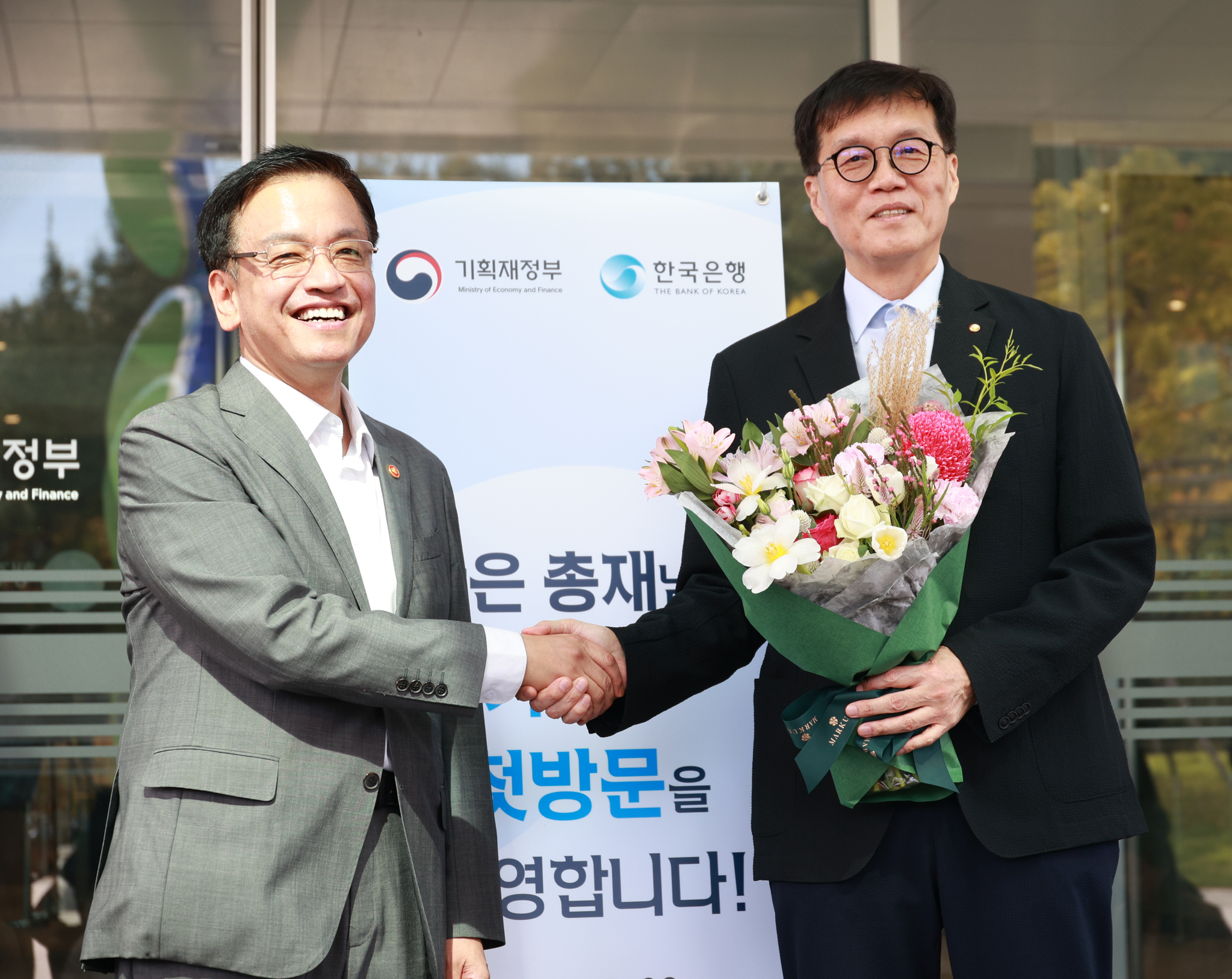 Minister of Economy and Finance Choi Sang-mok, left, shakes hands with Bank of Korea Gov. Rhee Chang-yong during Rhee's visit to the ministry's headquarters in Sejong on Monday. [MINISTRY OE ECONOMY AND FINANCE]