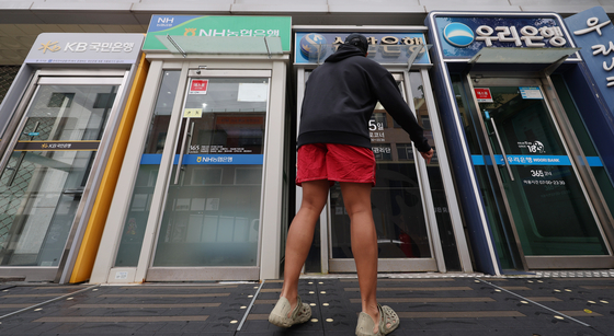 Pedestrians pass by ATMs from firms including KB Kookmin Bank and Woori Bank in Seoul on Tuesday. [YONHAP]