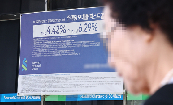 A woman passes by a banner that shows information about the bank's home equity loan program posted on the exterior of a bank in Seoul on Sept.22. [YONHAP]