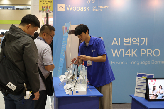 Attendees view a demo of an AI translation device during Travel Show 2024 at Coex in Gangnam District, southern Seoul, on Friday. [YONHAP]